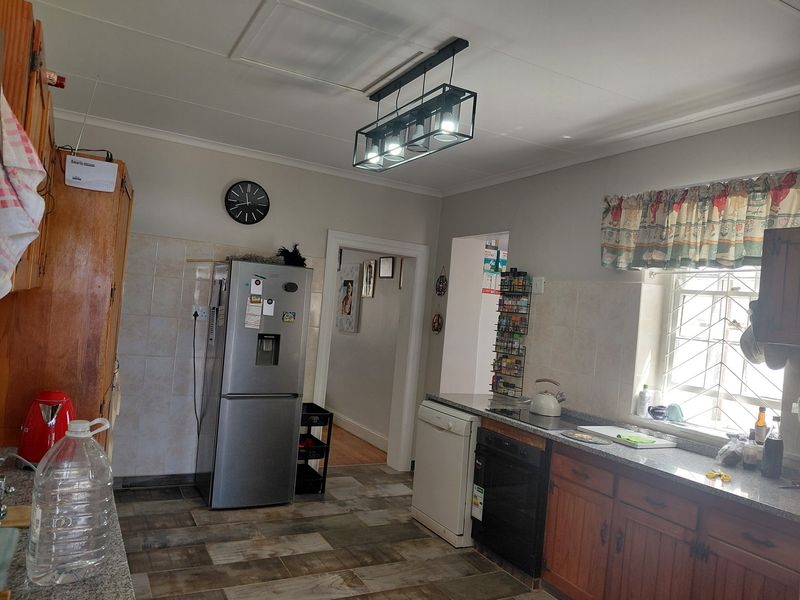 A functional kitchen featuring wooden cabinetry, granite countertops, tiled backsplash, and modern pendant lighting, with a window fitted with a security gate.