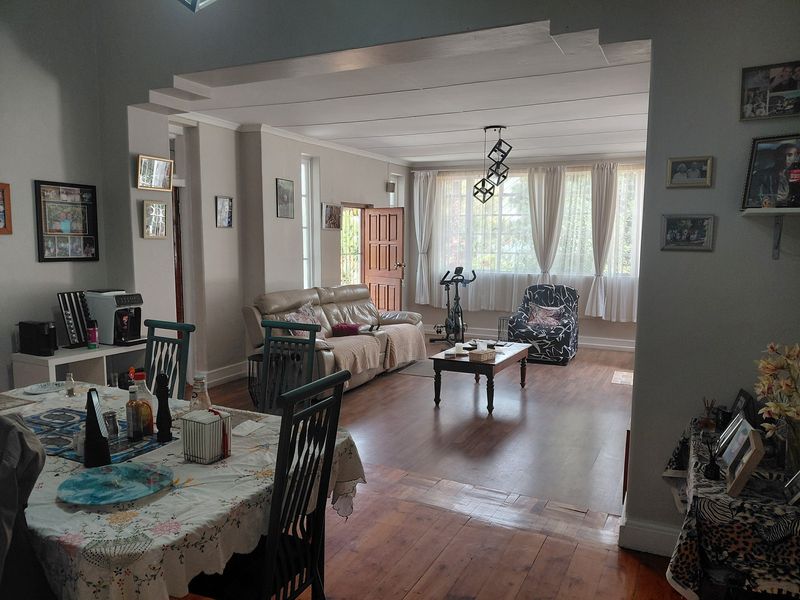 Spacious open-plan living and dining area featuring a mix of hardwood and laminate flooring, recessed ceiling details, and natural light through large windows.