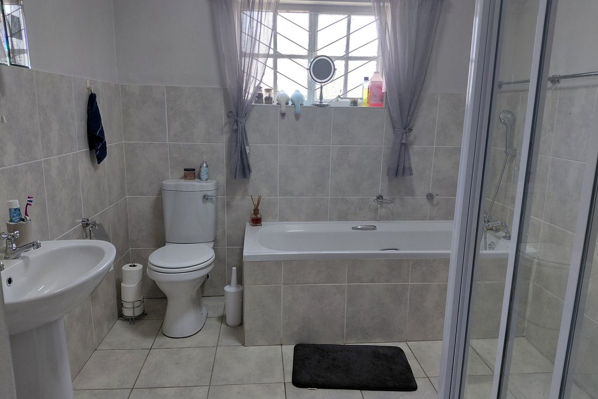 A functional bathroom featuring a pedestal basin, toilet, built-in bathtub, and a separate shower enclosure with neutral wall and floor tiling.