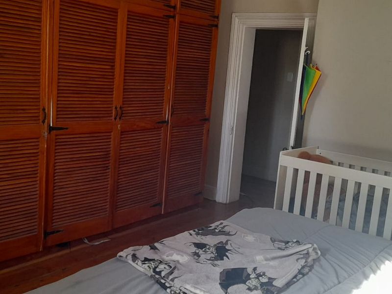 A bedroom featuring classic timber flooring and large built-in wooden louvered wardrobes, offering ample storage space.