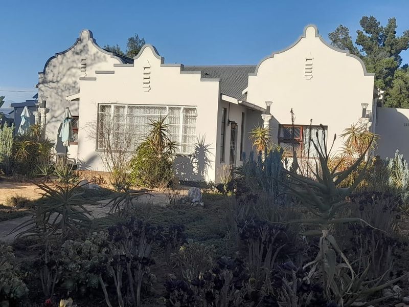 Front elevation of a house featuring distinctive gabled architecture, metal-framed windows, and an established garden with a concrete pathway.
