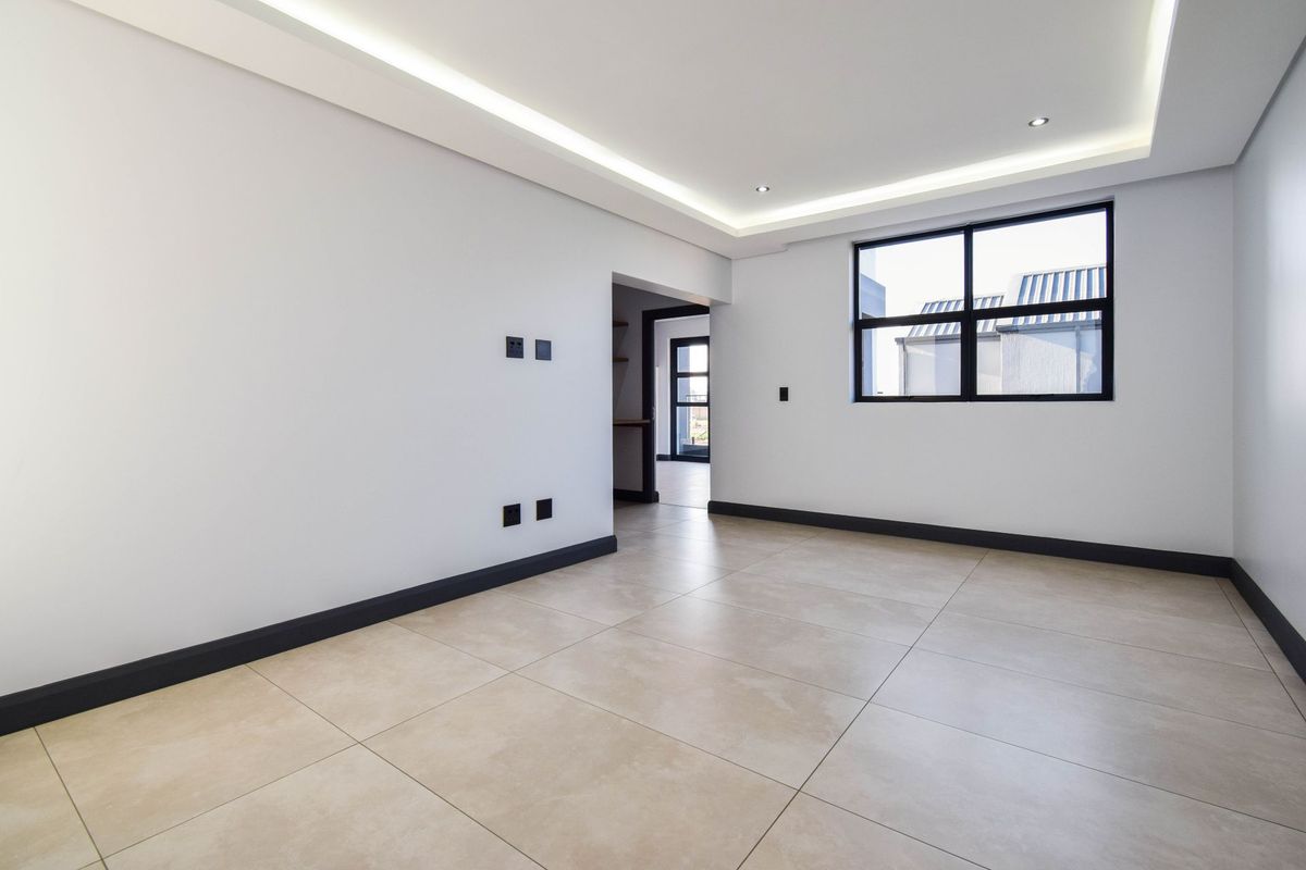 A bright, modern, and empty living room featuring large format floor tiles, recessed ceiling lighting, and dark window frames.