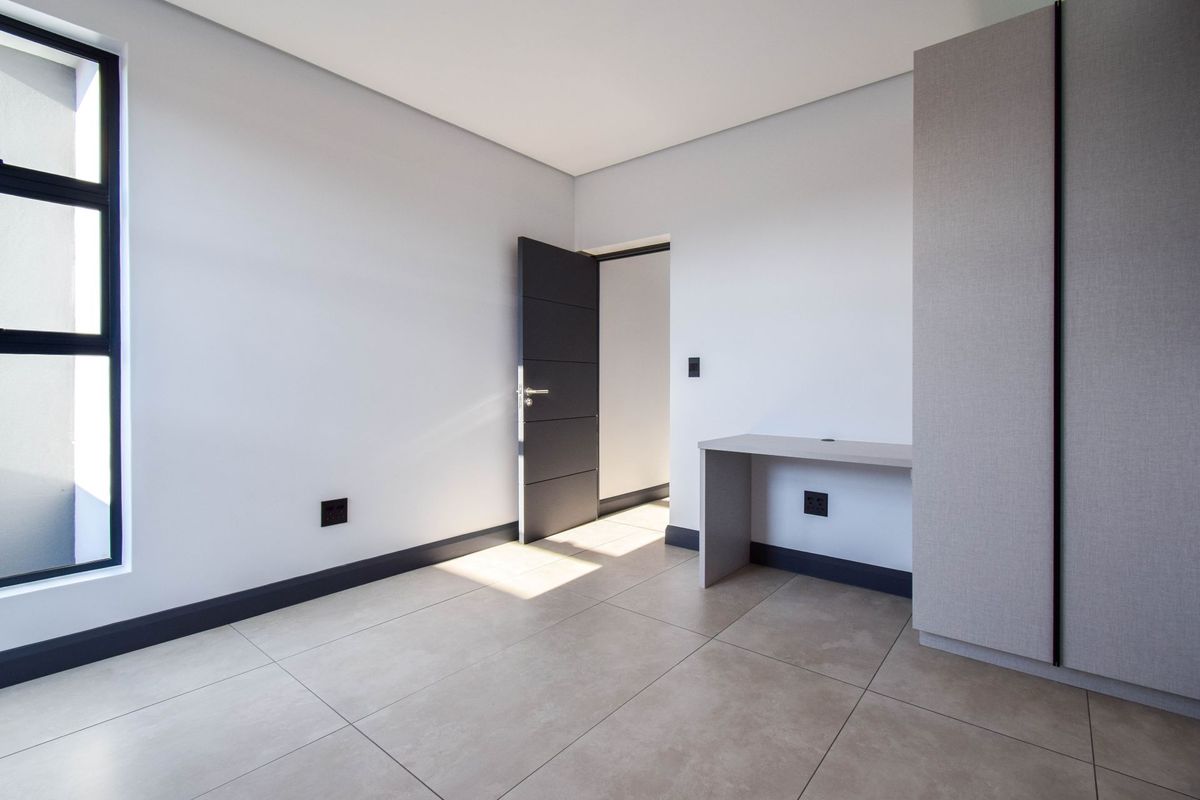 A modern, minimalist bedroom featuring neutral tiled flooring, built-in cabinetry, a sleek desk area, and a large window providing natural light.
