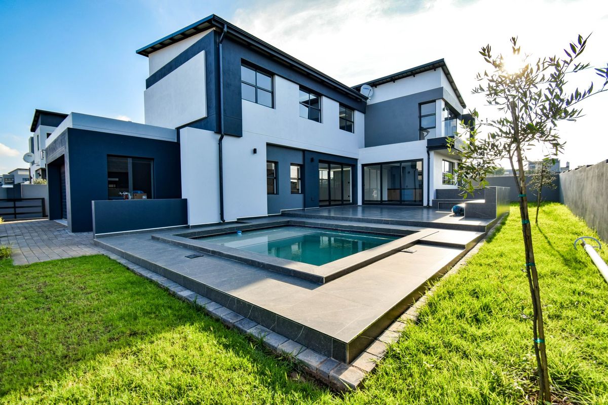 Modern double-story residence featuring a sleek rear facade, tiled patio area, and a built-in swimming pool set within a landscaped garden.