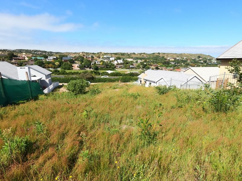 A vacant residential plot featuring a gentle slope, natural vegetation, and surrounding neighborhood views, ideal for future development.