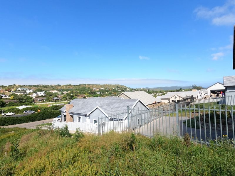 Elevated view of a residential area featuring modern homes with tiled roofs and secure perimeter fencing, set against a scenic landscape.