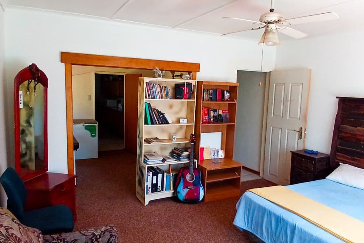 A bedroom featuring carpeted flooring, a ceiling fan, and an open doorway leading to an adjacent utility area.