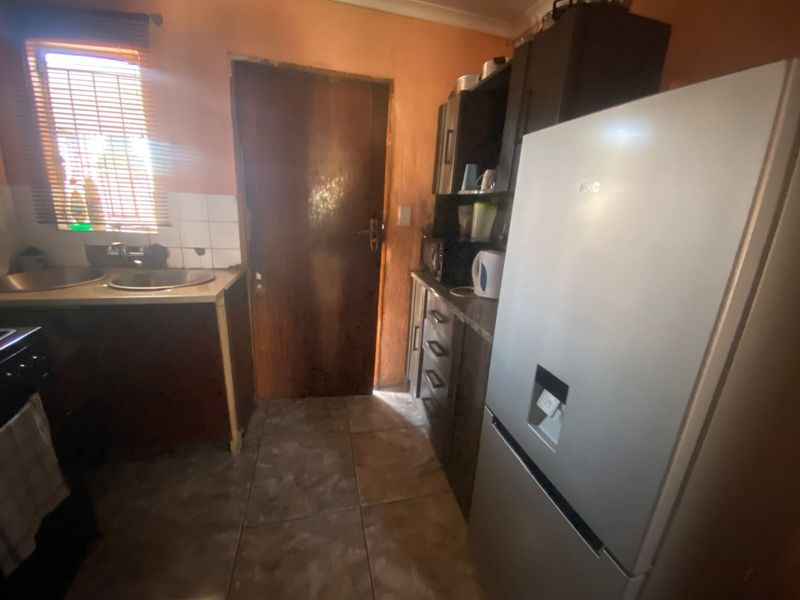 A compact kitchen featuring dark cabinetry, tiled flooring, and a stainless steel sink, providing a functional workspace with direct access to an exterior door.