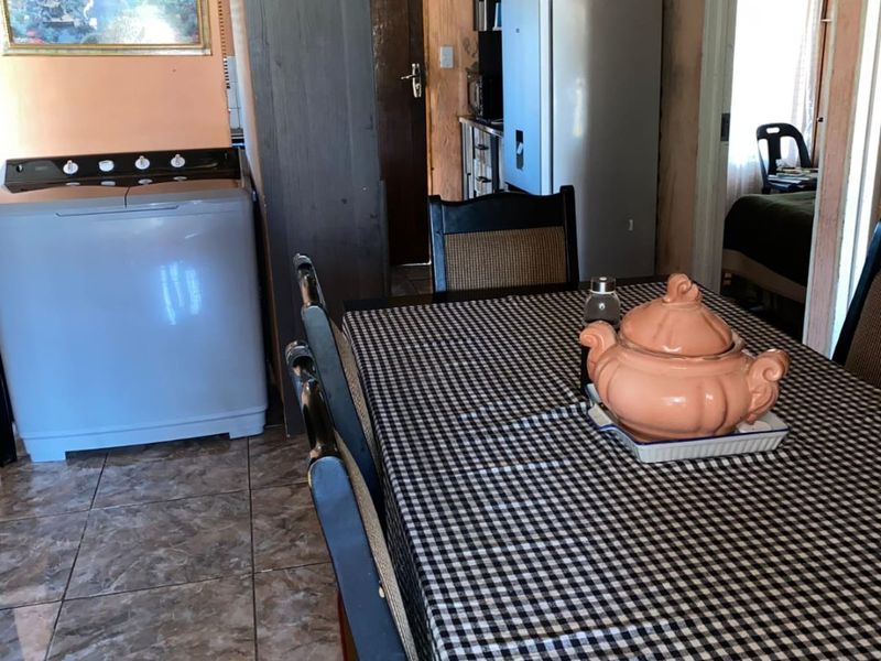 A multi-functional living and dining area featuring tiled flooring and direct access to adjacent rooms, showing signs of wear and dated finishes.