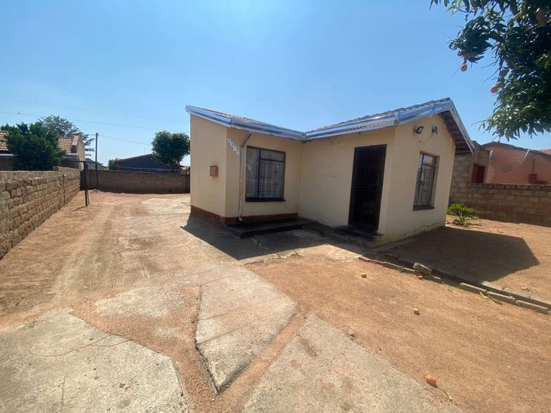 Front view of a single-story house featuring a concrete driveway, perimeter boundary wall, and metal security bars on windows and doors.