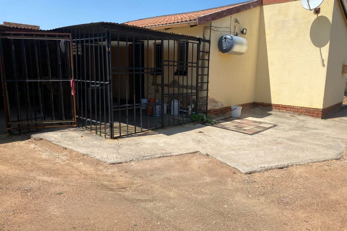 Rear exterior view of the property featuring a concrete patio area, metal security enclosure, and external geyser unit.