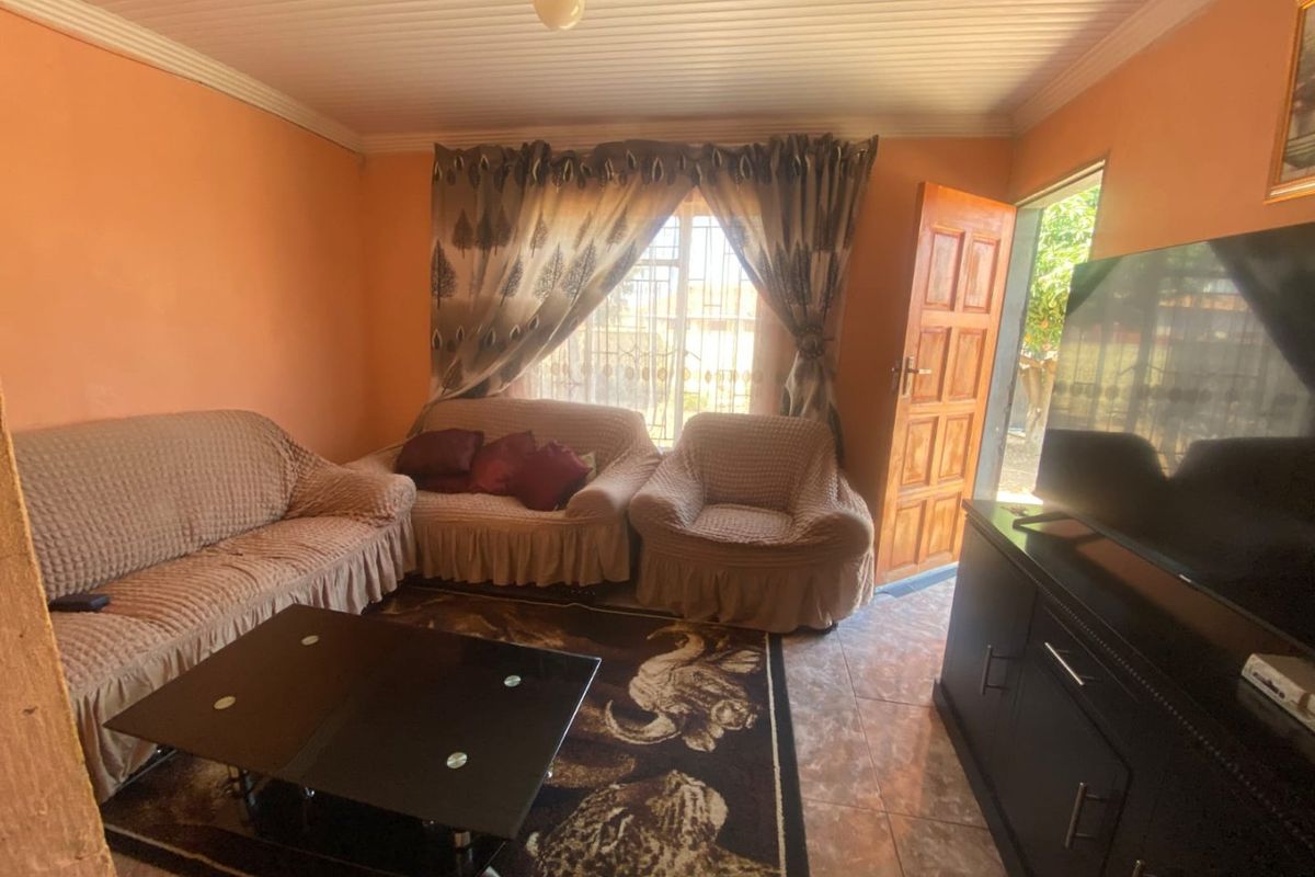 A living room featuring tiled flooring, a wooden entrance door, and a window with security bars, providing access to the exterior.