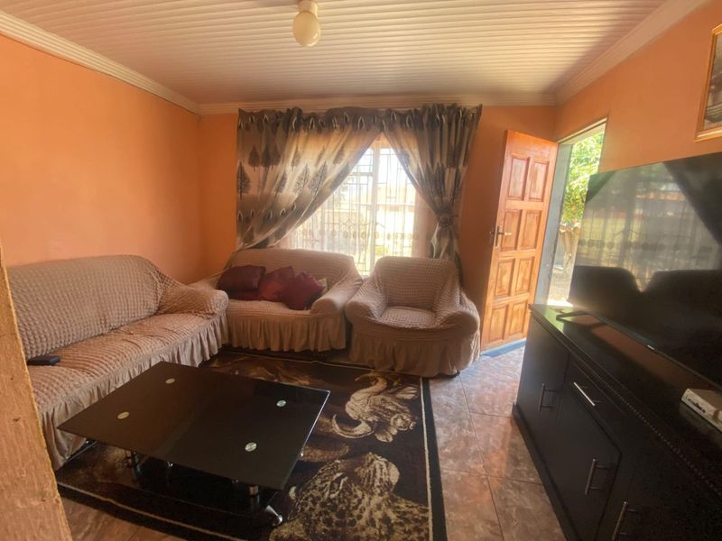 A living room featuring tiled flooring, a wooden entrance door, and a window with security bars, providing access to the exterior.