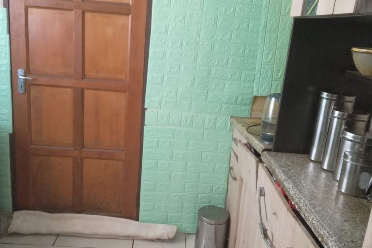 A kitchen area featuring light wood-toned cabinetry, granite-style countertops, and distinctive green textured wall paneling with tiled flooring.