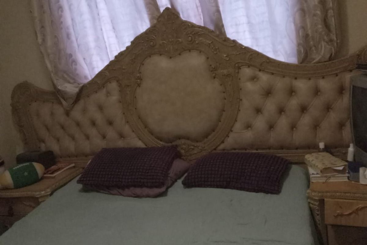 A bedroom featuring a large ornate tufted headboard and matching bedside tables positioned against a window with curtains.