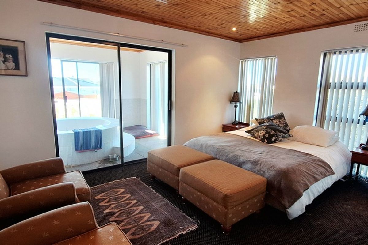 Spacious bedroom featuring a timber-clad ceiling, vertical blinds, and sliding glass doors leading to an adjoining area with a built-in circular bathtub.
