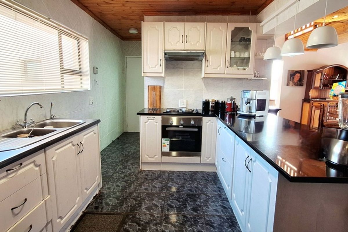 A functional kitchen featuring white cabinetry, dark countertops, a built-in oven, hob, extractor fan, and a double sink with a timber-paneled ceiling.