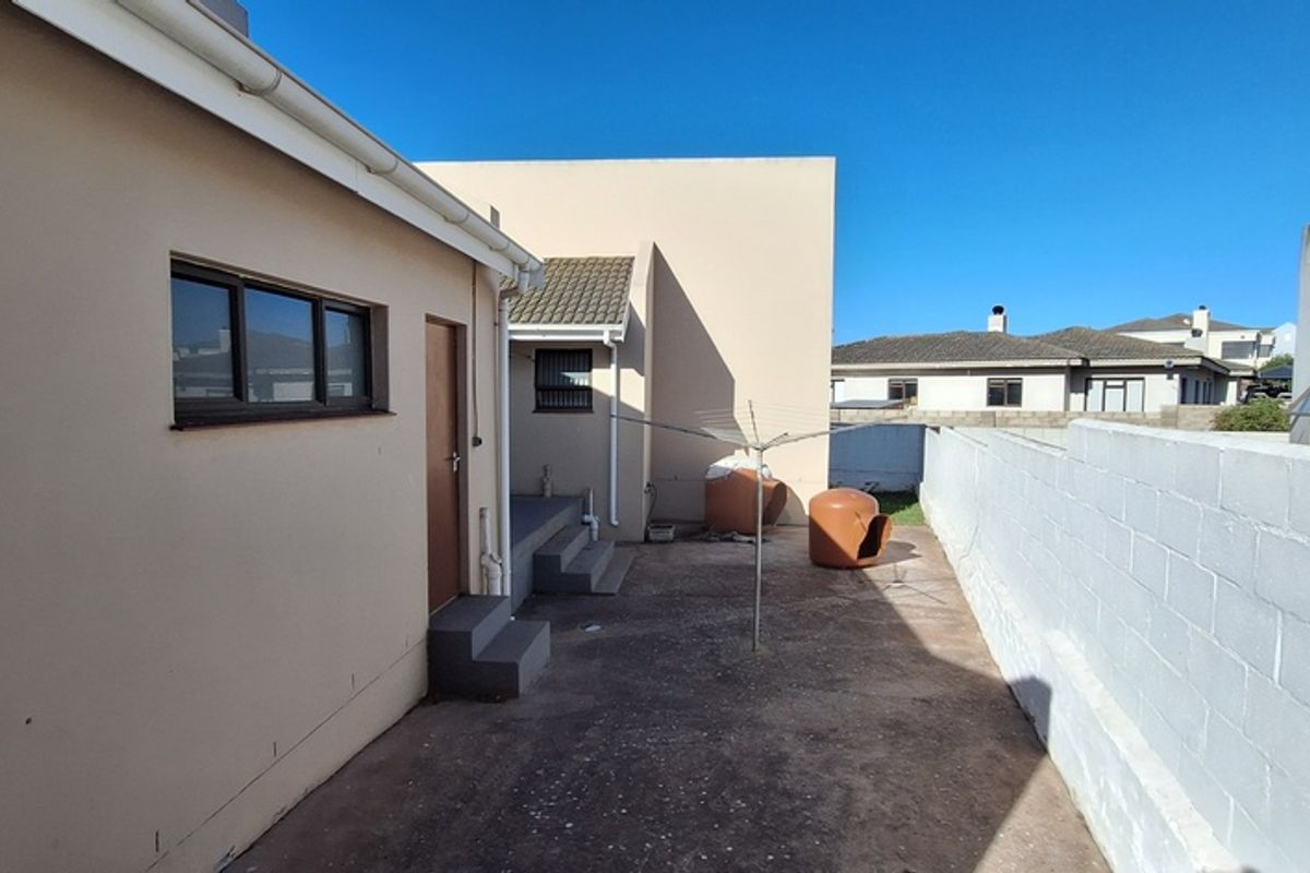 A rear exterior view of the property featuring a concrete courtyard, perimeter boundary wall, and access to the side of the house.