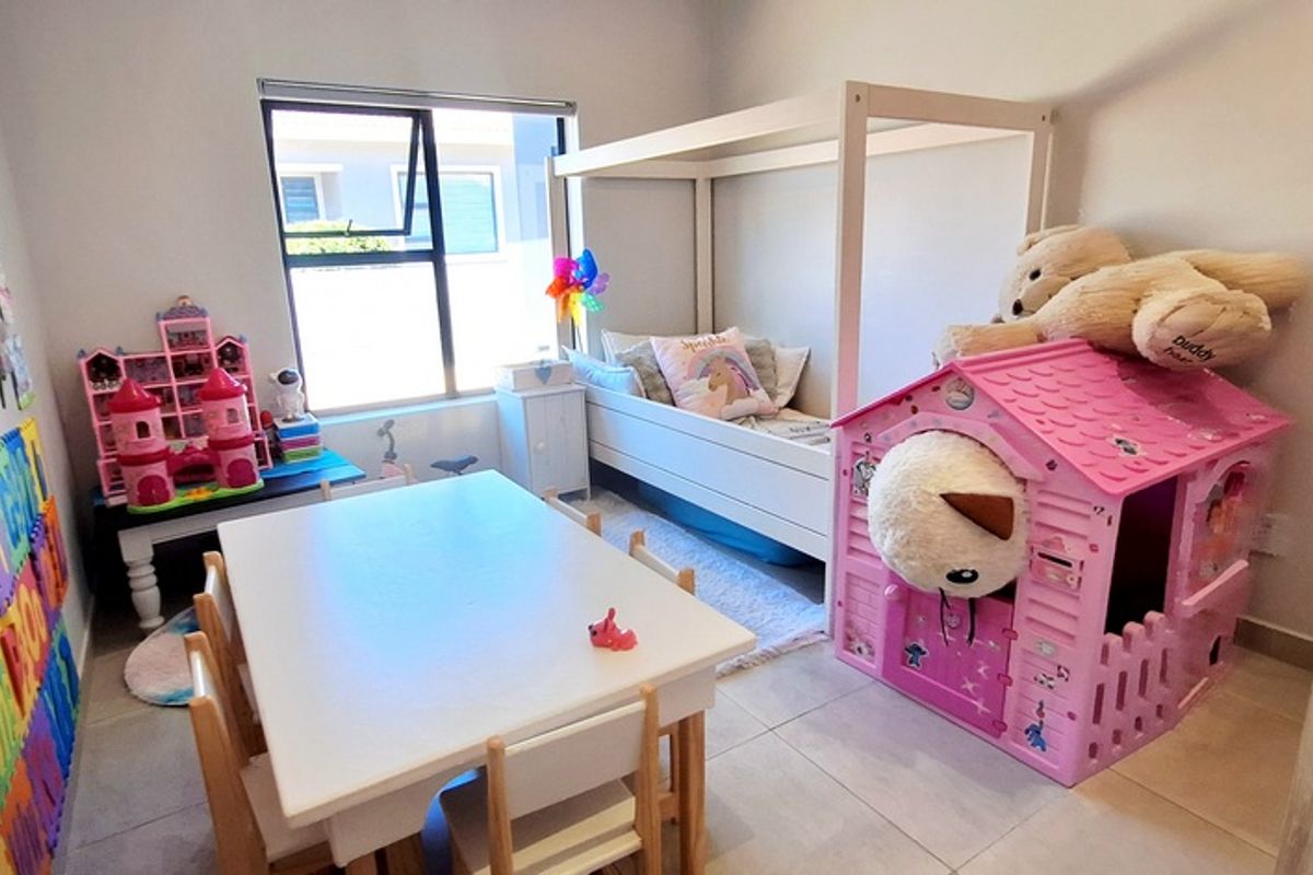 A bright bedroom featuring tiled flooring and a large window, currently utilized as a children's play and sleeping area.