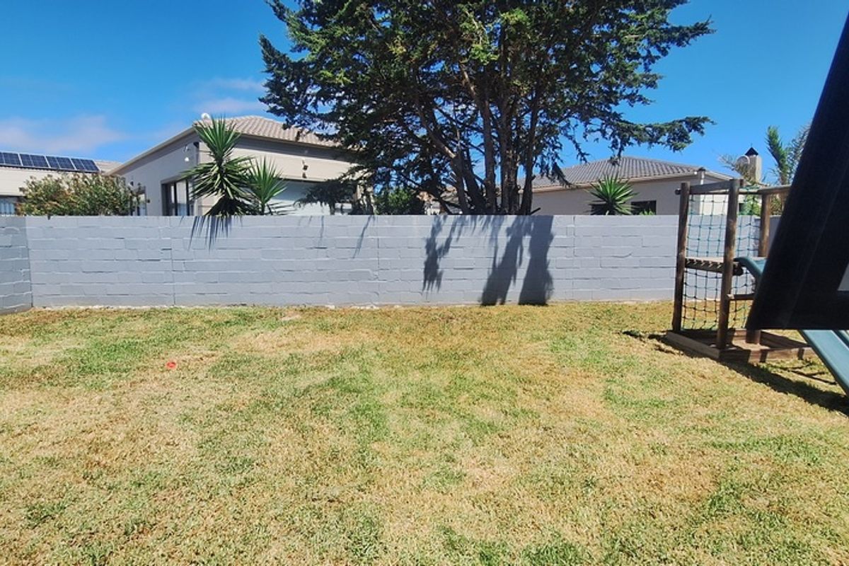 A private rear garden featuring a level lawn area enclosed by a painted masonry boundary wall.