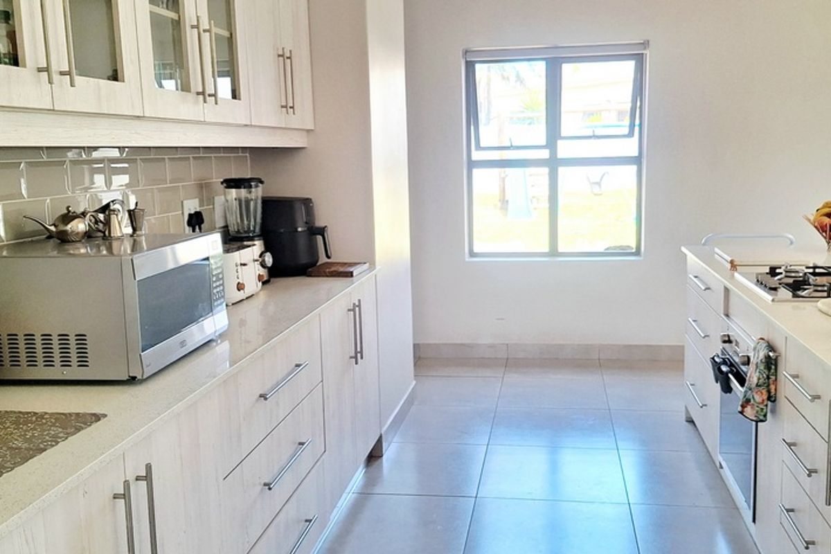 Modern kitchen featuring light wood-grain cabinetry, stone countertops, subway tile backsplash, built-in oven, and gas hob on a central island.