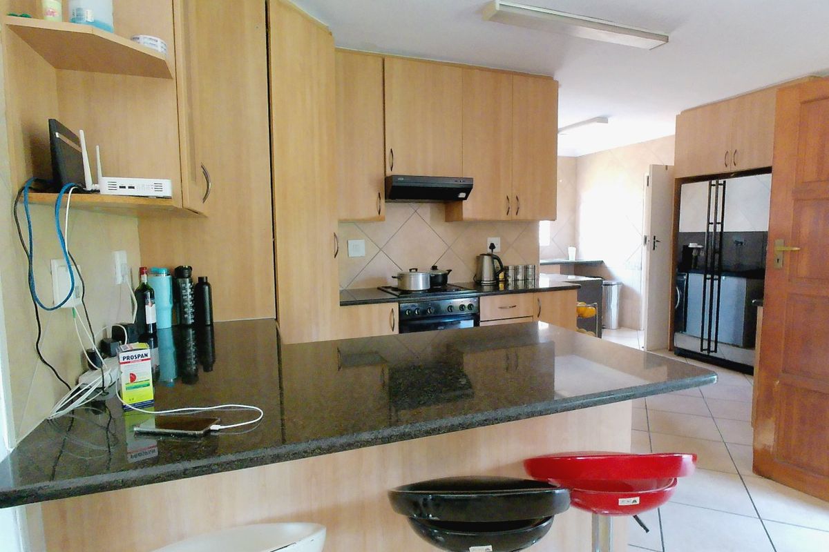 A functional kitchen featuring light wood cabinetry, dark granite countertops, a breakfast bar, and a built-in hob with an extractor fan.