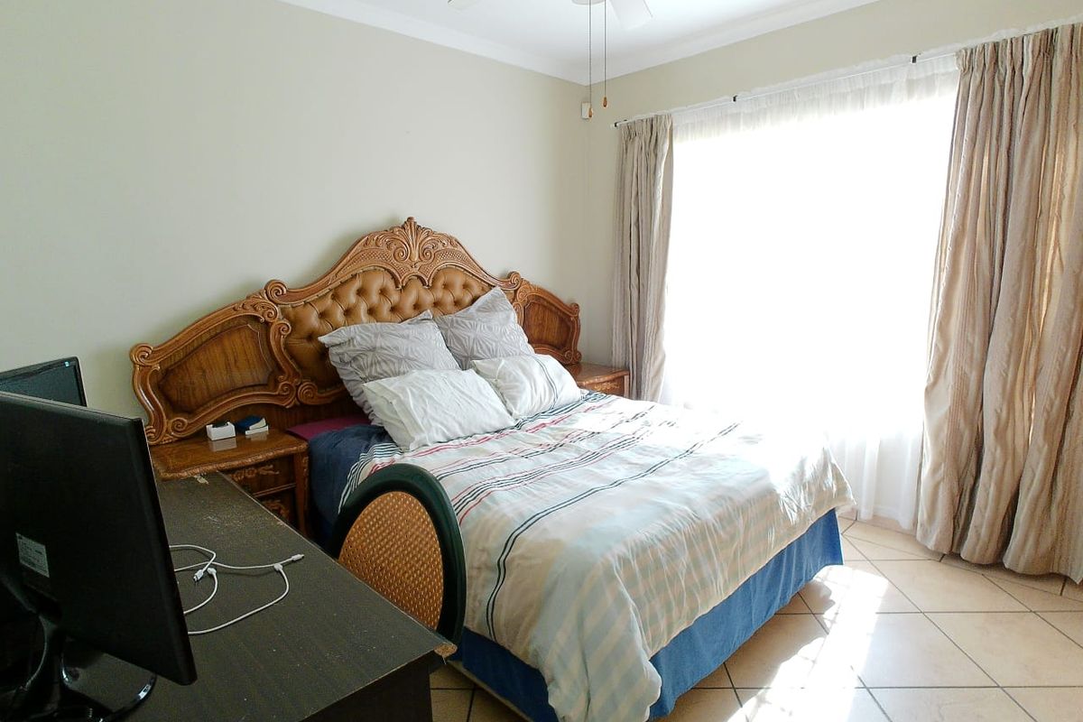 A well-lit bedroom featuring tiled flooring, a ceiling fan, and large windows with curtains, providing a comfortable and functional living space.