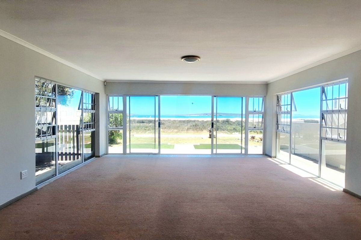 Spacious, light-filled living area featuring expansive glass sliding doors that offer panoramic coastal views and direct access to the outdoors.
