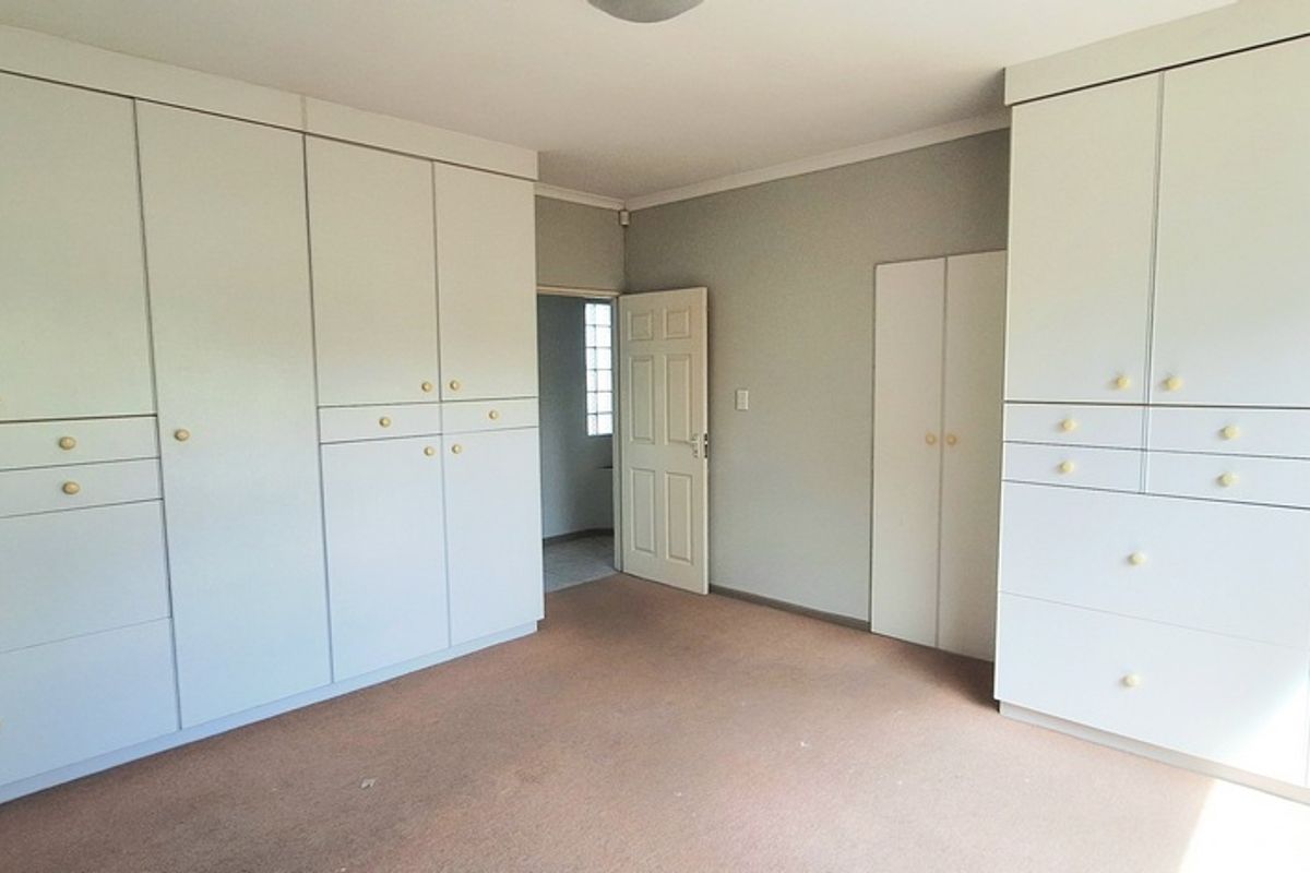 A spacious bedroom featuring extensive built-in cabinetry with ample storage, neutral wall finishes, and carpeted flooring.
