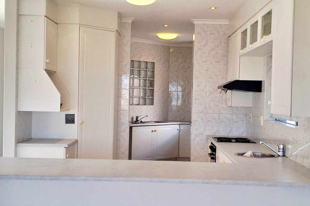 A functional kitchen featuring a breakfast bar, built-in cabinetry, integrated hob, extractor fan, and a secondary prep sink area with glass block accents.