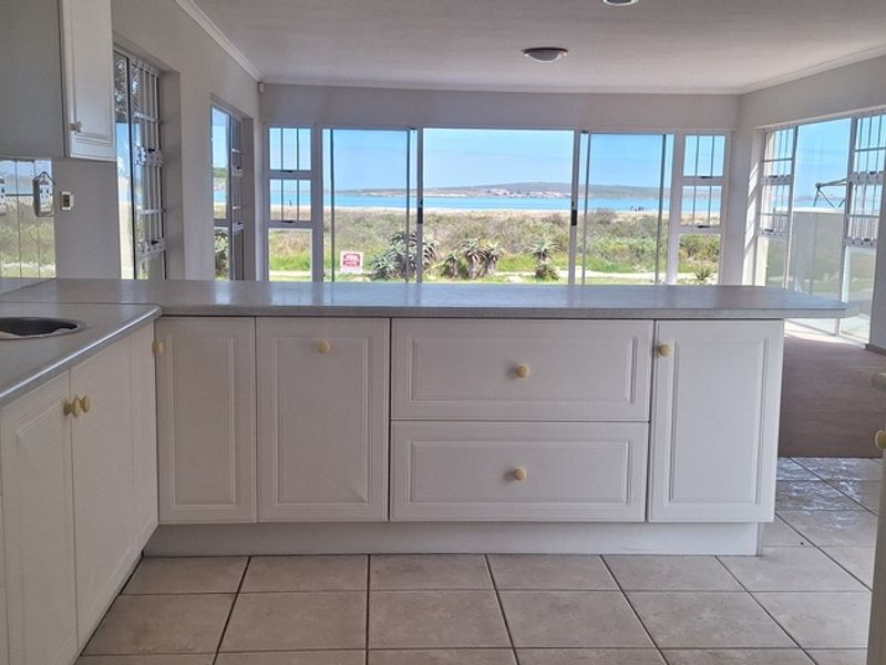 Open-plan kitchen featuring white cabinetry, laminate countertops, and a built-in oven, with expansive windows offering scenic coastal views.