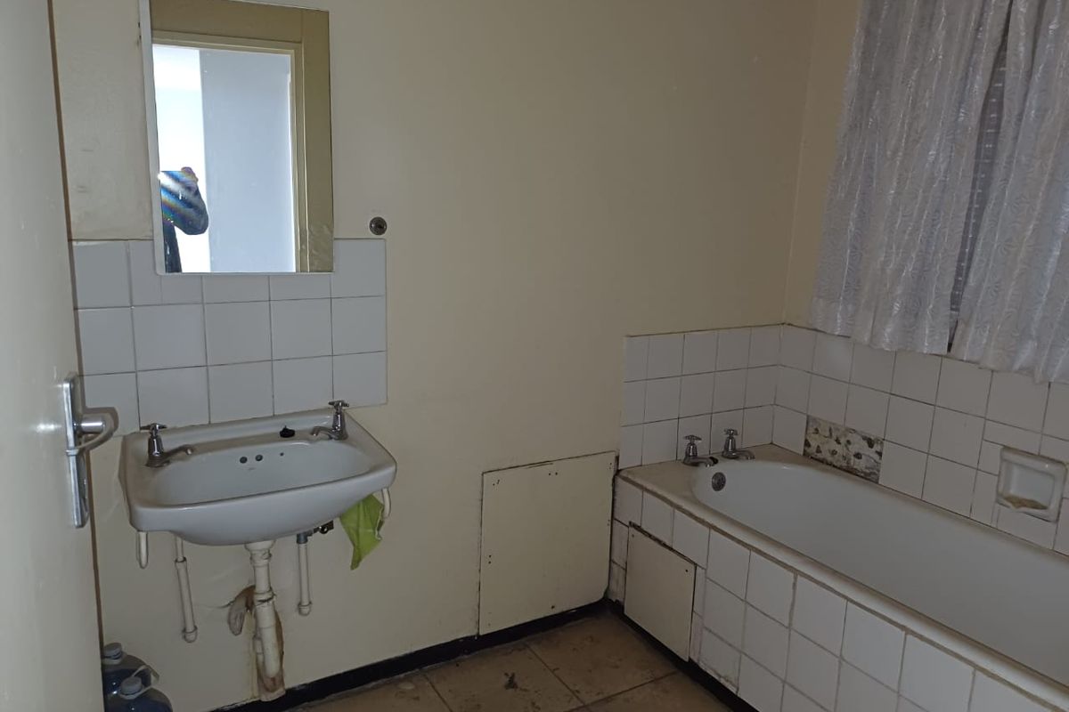 A dated bathroom featuring a standard bathtub, wall-mounted basin, and tiled splashbacks, requiring significant renovation and modernization.