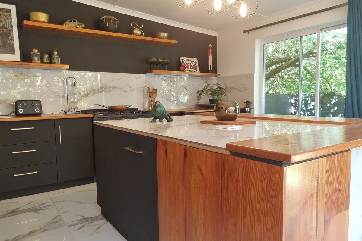 Modern kitchen featuring a large island with timber and marble-look finishes, sleek dark cabinetry, floating shelves, and marble-look floor tiles with garden access.