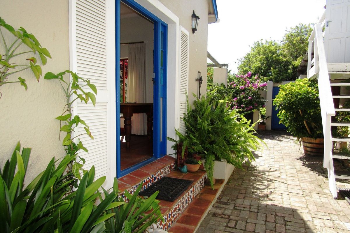 A charming rear courtyard entrance featuring a blue-framed doorway, decorative tiled steps, and brick paving, leading into the home.