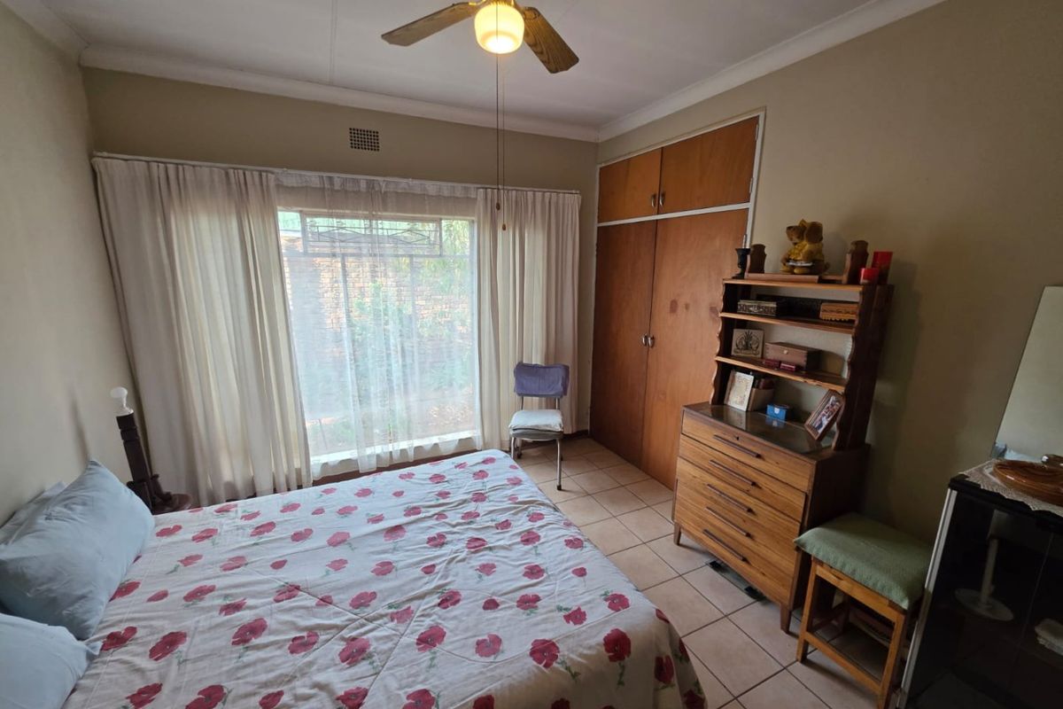 A bedroom featuring built-in wooden cupboards, tiled flooring, and a ceiling fan, offering a functional space with natural light.