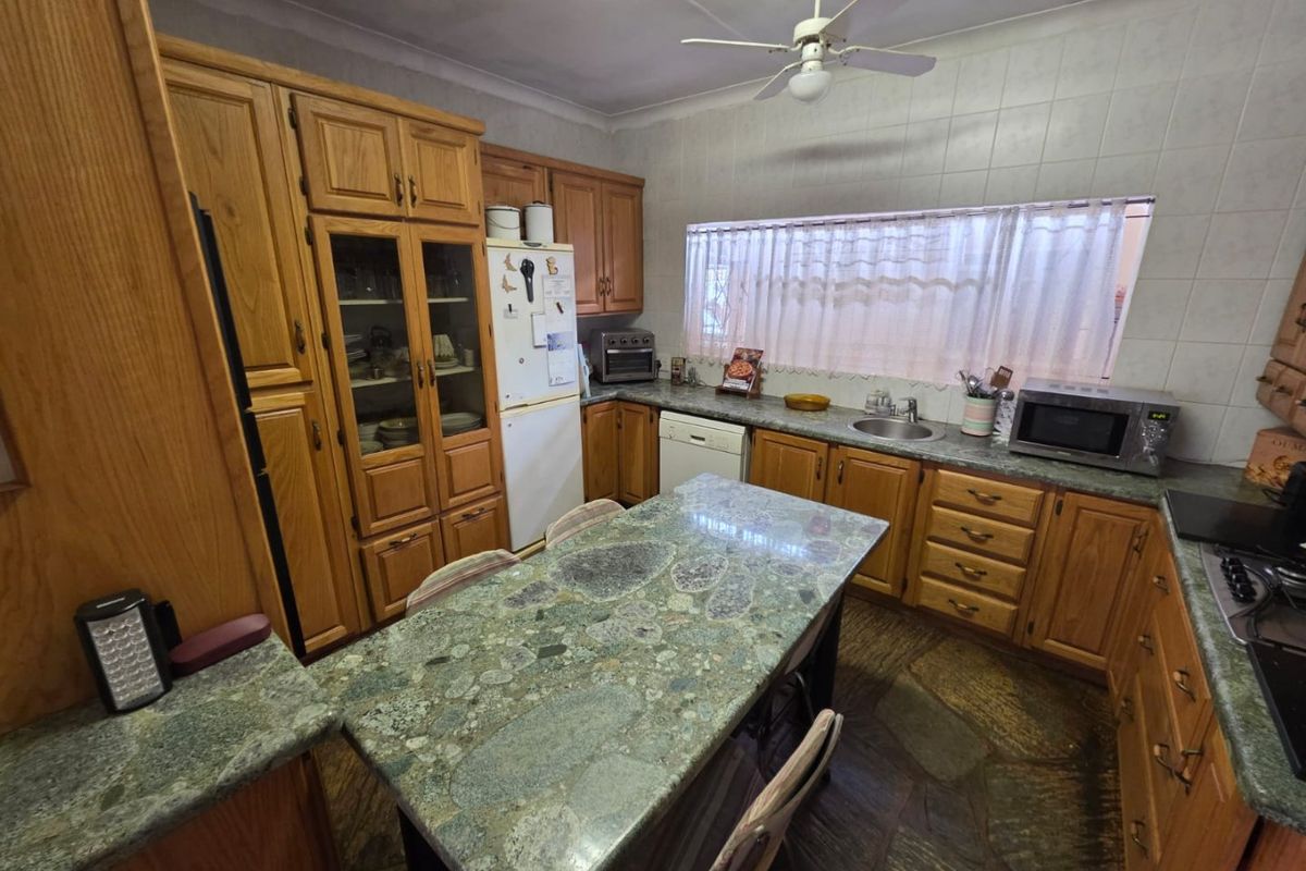 A traditional kitchen featuring solid wood cabinetry, a large stone-topped island, and stone flooring, offering a functional layout with ample storage space.
