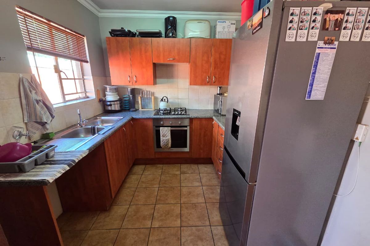 A functional kitchen featuring wooden cabinetry, granite-look countertops, a built-in oven with gas hob, and a double stainless steel sink.