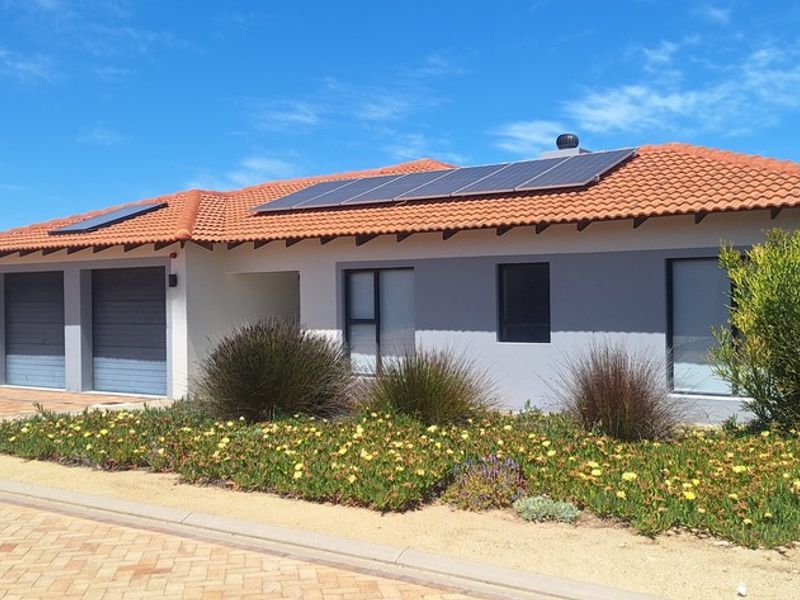 A well-maintained single-story home featuring a terracotta tiled roof, solar panels, a double garage, and a neat front garden with a paved driveway.
