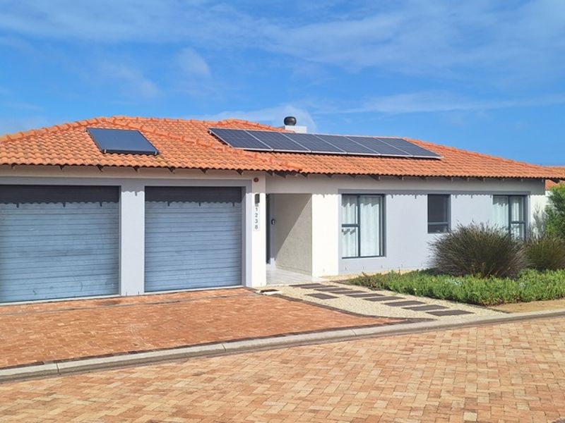 Front elevation of a single-story house featuring a double garage, solar panels, solar geyser, and a well-maintained paved driveway and garden.