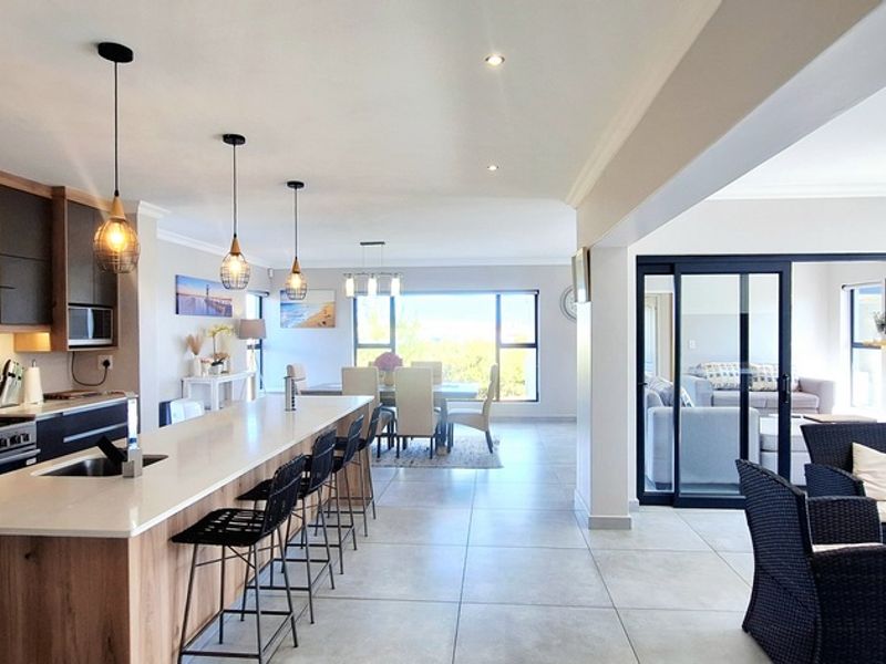 Spacious open-plan kitchen and living area featuring a large island, modern cabinetry, stone countertops, and seamless flow to an outdoor patio through sliding doors.