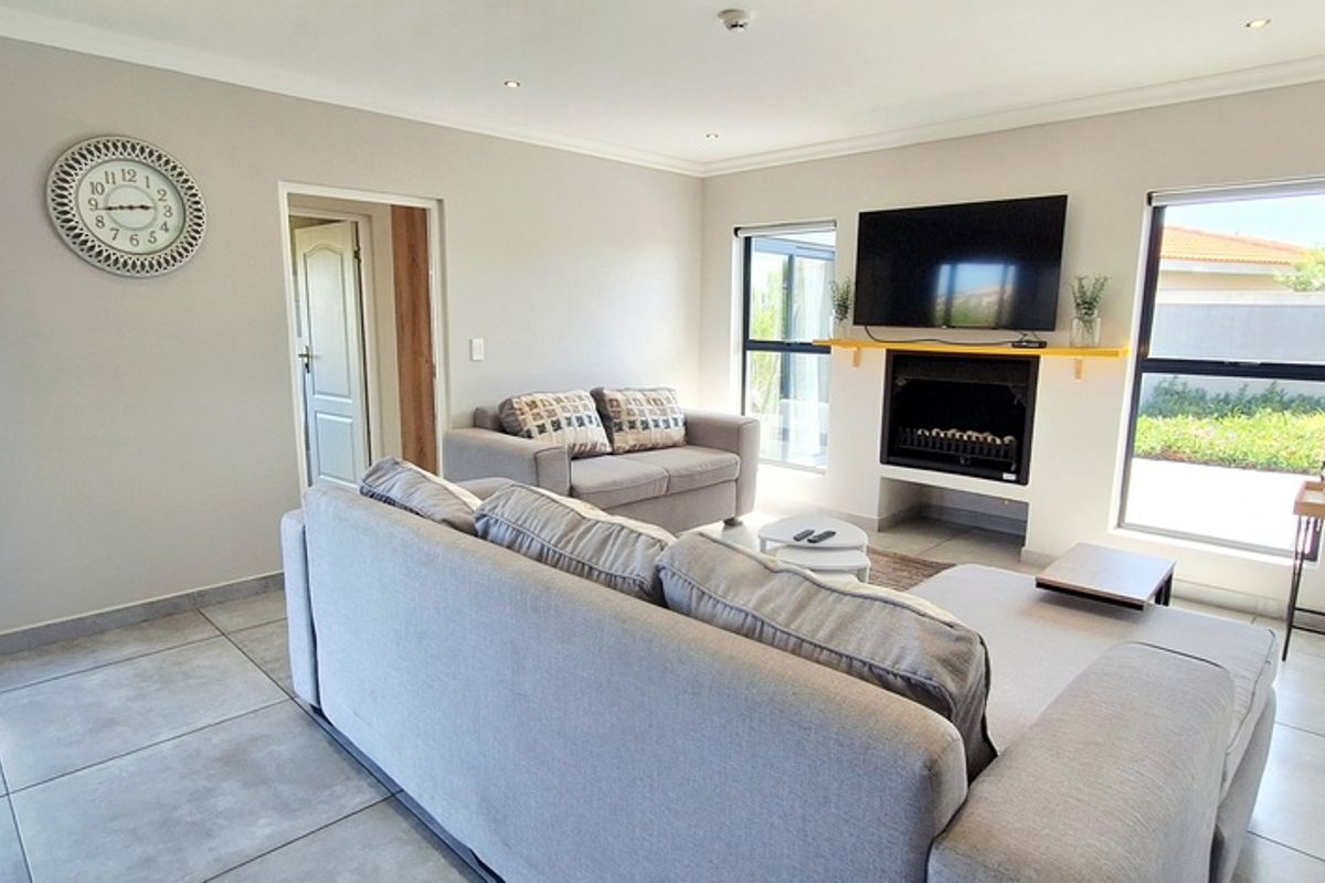 A bright and modern living room featuring large windows, tiled flooring, recessed lighting, and a built-in fireplace with a mounted television.