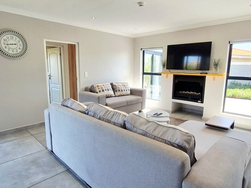 A bright and modern living room featuring large windows, tiled flooring, recessed lighting, and a built-in fireplace with a mounted television.