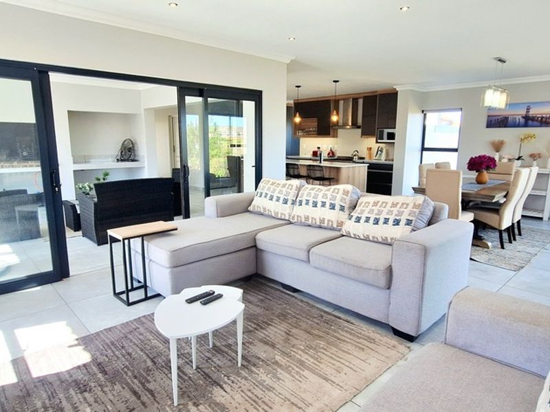 Spacious open-plan living area featuring modern tiled floors, recessed lighting, and seamless flow to an enclosed patio, adjacent to a contemporary kitchen.