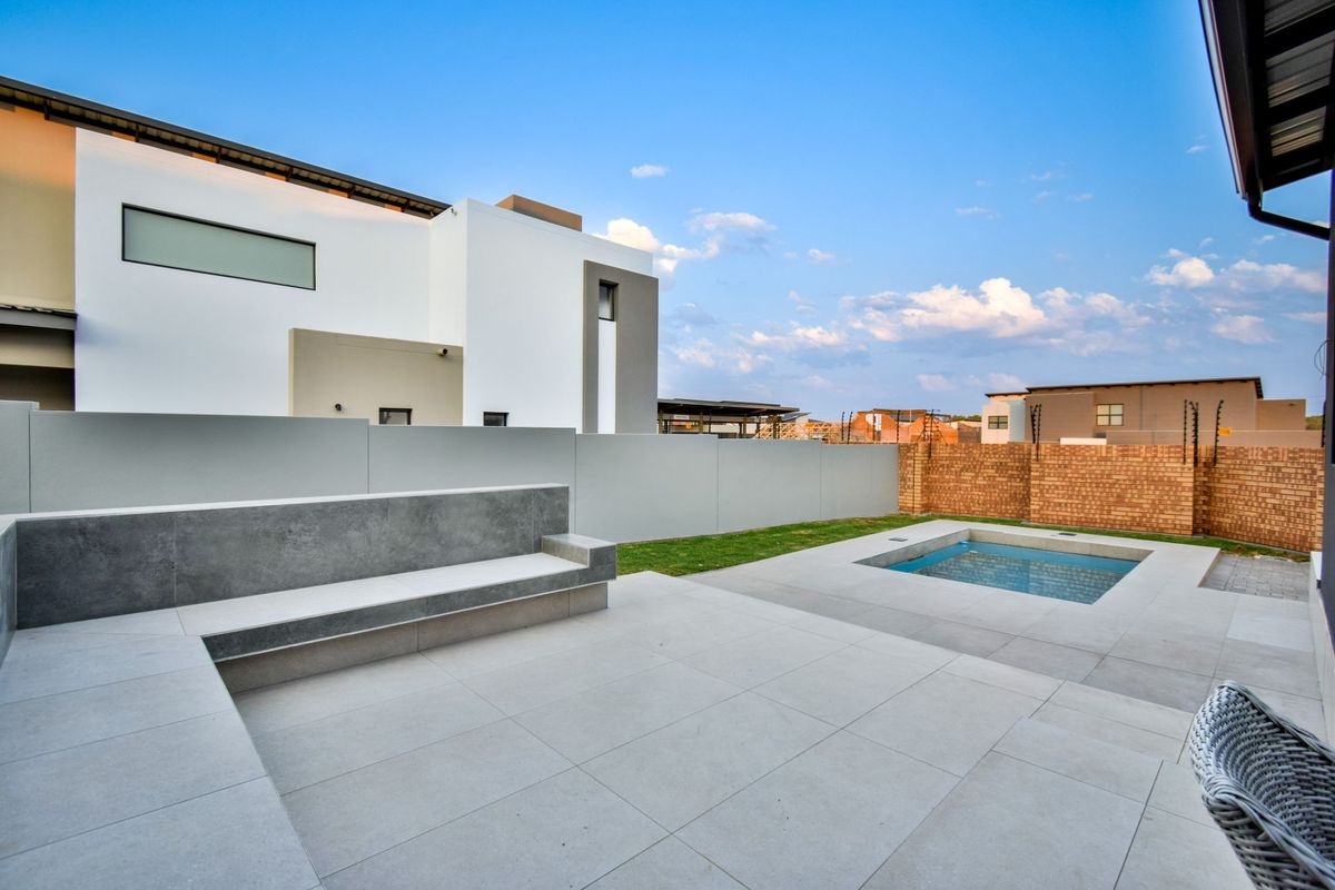 Modern rear garden featuring a tiled patio with built-in concrete bench seating, a small plunge pool, and perimeter walling.