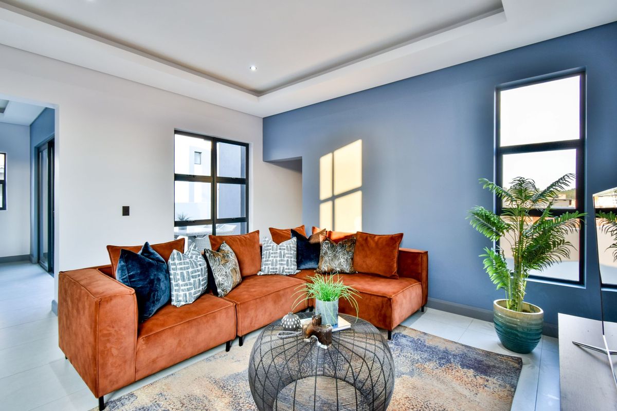 A bright and modern living room featuring a tray ceiling, large windows with black frames, and tiled flooring.