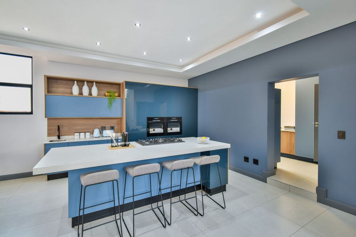 Modern kitchen featuring a large central island with a built-in gas hob, sleek blue cabinetry, integrated double ovens, and recessed ceiling lighting.
