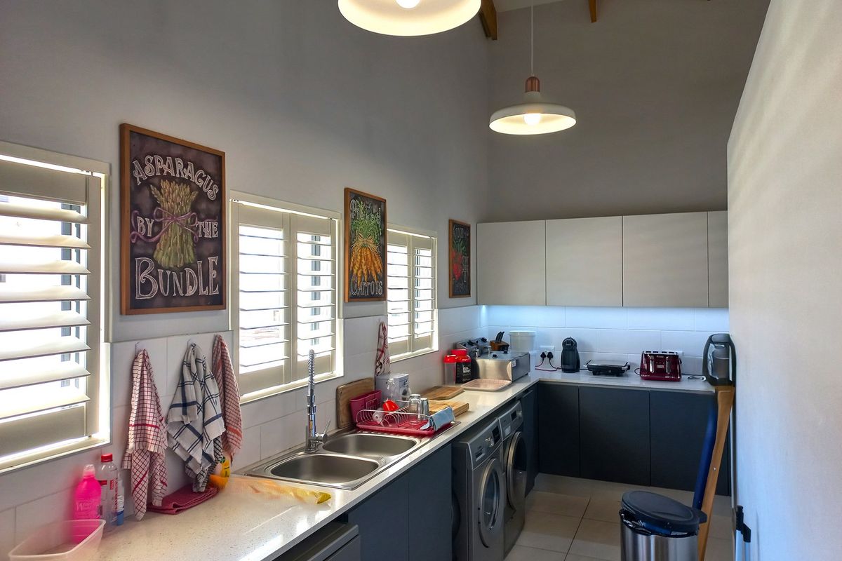 Modern kitchen featuring sleek cabinetry, integrated appliances, double sink, and plantation shutters, set under a high vaulted ceiling with pendant lighting.