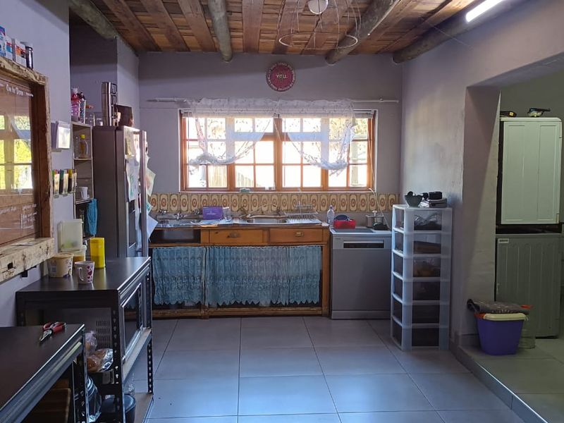 A rustic kitchen featuring timber ceiling beams, tiled flooring, and a double basin sink with a tiled splashback.