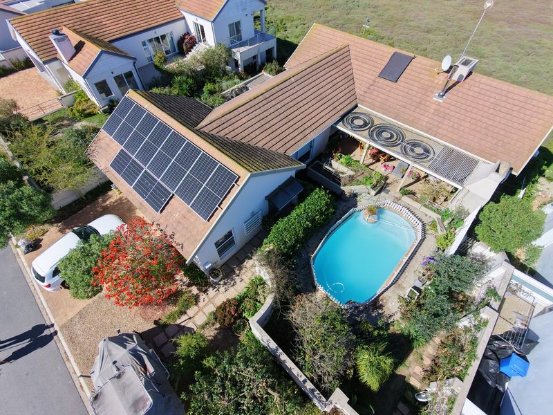 Aerial view of a residential property featuring a swimming pool with solar heating, rooftop solar panels, and a paved outdoor entertainment area.