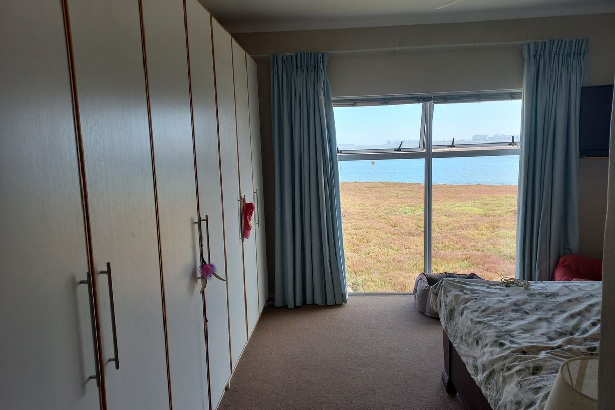 A bedroom featuring extensive built-in cupboards, a ceiling fan, and a large window offering scenic water views.